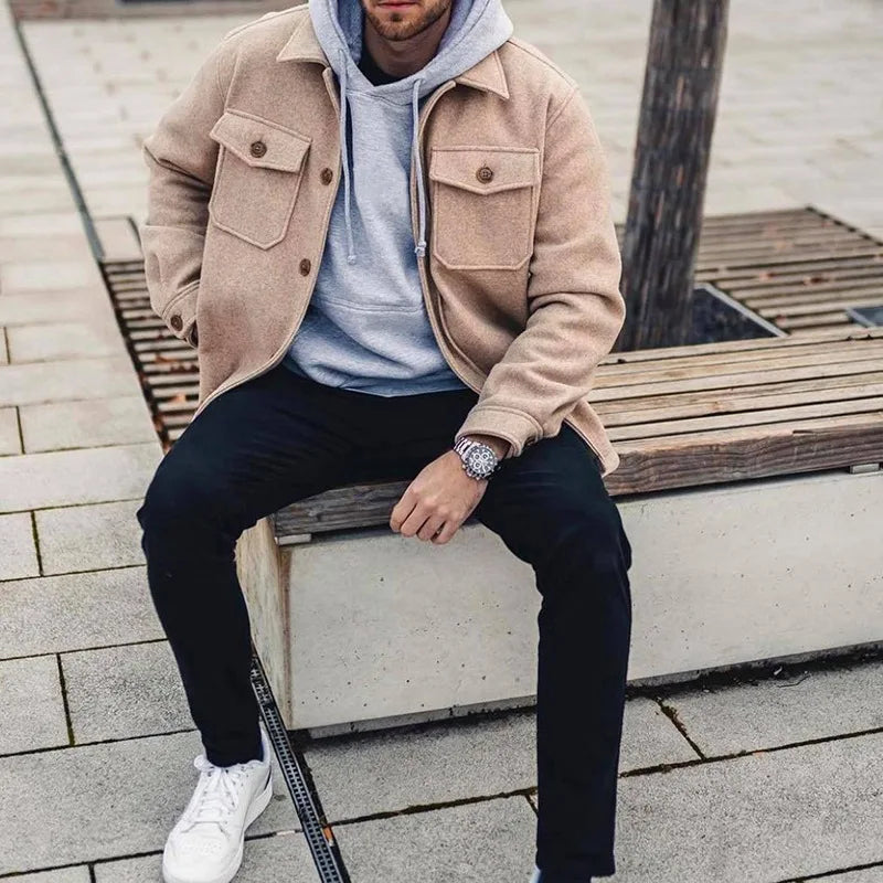 Mann trägt stylischen Designermantel während er auf einer Bank sitzt