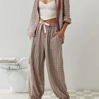 Eine Frau trägt ein 2-teiliges braunes lässiges Pyjama-Set mit kariertem Design und weißem Innenoberteil