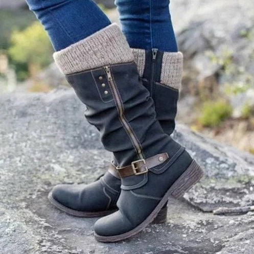 Eine Nahaufnahme eines schwarzen orthopädischen Stiefels mit lässigem Design und Strickbund, der von einer Person getragen wird, die auf felsigem Boden steht. Das Bild hebt sein stilvolles Aussehen und seine Komfortmerkmale hervor.