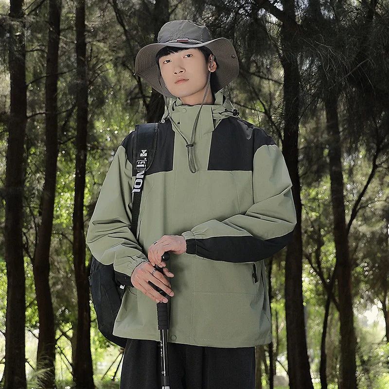 Ein Mann trägt eine grüne wind- und wasserdichte Outdoor-Kapuzenjacke mit langen Ärmeln und farblich abgestimmtem Reißverschluss