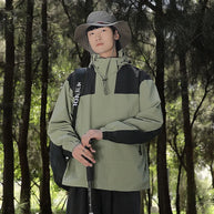 Ein Mann trägt eine grüne wind- und wasserdichte Outdoor-Kapuzenjacke mit langen Ärmeln und farblich abgestimmtem Reißverschluss
