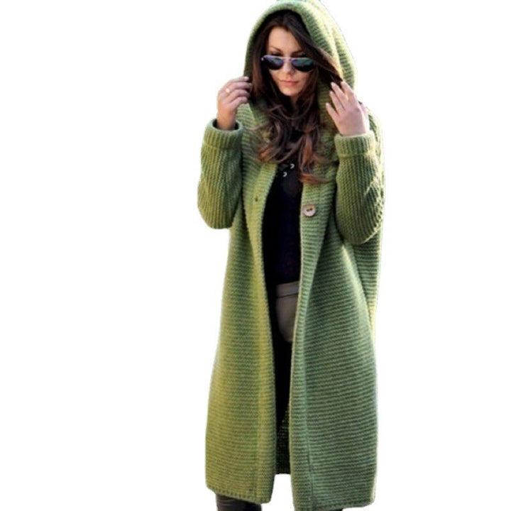Eine Frau trägt eine lange grüne Strickjacke mit Kapuze auf weißem Hintergrund