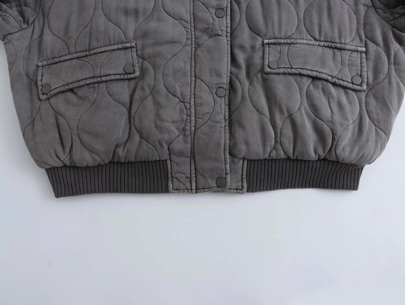 Eine Nahaufnahme des Saums und der Manschetten einer grauen Bomberjacke, die ihr strukturiertes Design zeigt.