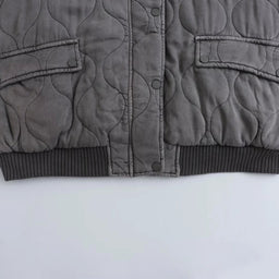 Eine Nahaufnahme des Saums und der Manschetten einer grauen Bomberjacke, die ihr strukturiertes Design zeigt.
