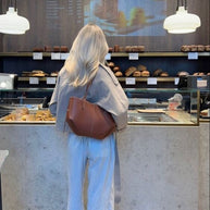 Eine frau mit langen haaren steht an einem café-theke mit einer braun ledertasche