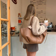 Eine frau mit einer braun ledertasche und einem kaffee steht an der cafétheke