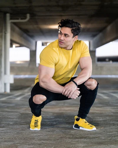 Mann trägt ein gelbes T-Shirt, dazu eine schwarze Hose und gelbe Turnschuhe, sitzt in geduckter Position