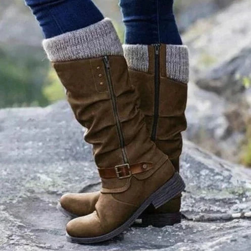 Eine Nahaufnahme eines braunen orthopädischen Stiefels mit lässigem Design und Strickbund, der von einer Person getragen wird, die auf felsigem Boden steht und sein stilvolles Aussehen und seine Komfortmerkmale hervorhebt.