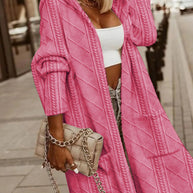 Modische Frau trägt eine rosa Strickjacke, ein weißes bauchfreies Top und blaue Jeans und hält eine beige gesteppte Handtasche mit Kette