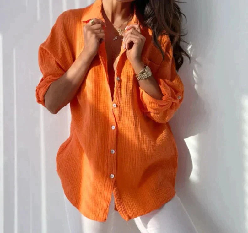 Frau in orangefarbener Bluse hält ihren Kragen vor eine weiße Wand