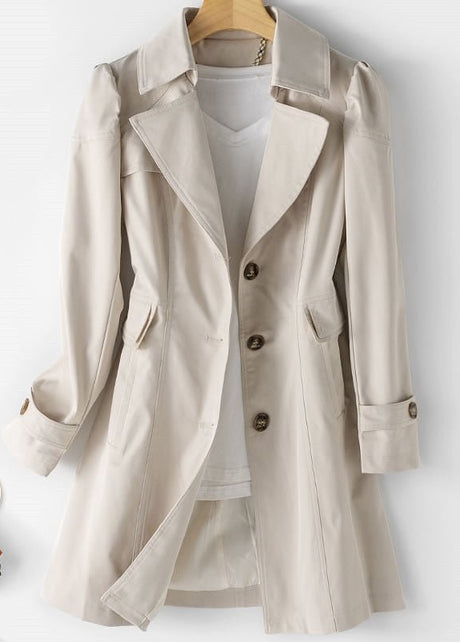 Elegante beige mittellange Jacke auf weißem Hintergrund mit Knopfleiste und stilvollem Kragen, ergänzt durch ein orangefarbenes Accessoire.