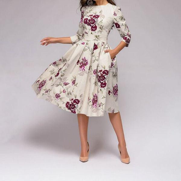 Frau posiert auf einem grauen Hintergrund in einem weißen, eleganten, mittellangen Retrozo-Kleid