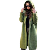 Eine Frau trägt eine lange grüne Strickjacke mit Kapuze auf weißem Hintergrund