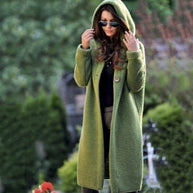 Eine Frau trägt eine lange grüne Strickjacke mit Kapuze auf weißem Hintergrund