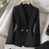 Ein schwarzer Blazer mit maßgeschneidertem Design und goldenen Knöpfen, präsentiert auf einer weichen Oberfläche neben einer kleinen Handtasche.