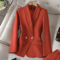 Ein leuchtend gold-orangefarbener Blazer mit maßgeschneiderter Passform und goldenen Knöpfen, präsentiert auf einer weichen Oberfläche neben einer passenden Hose und einer kleinen Handtasche.