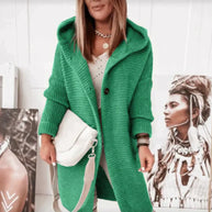 Eine Person trägt eine lange grüne Strickjacke mit Kapuze und zwei schwarzen Knöpfen und hält eine Tasche