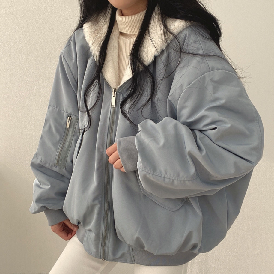 Eine Frau trägt eine blaue Wendejacke mit Kapuze, Reißverschluss und Tasche