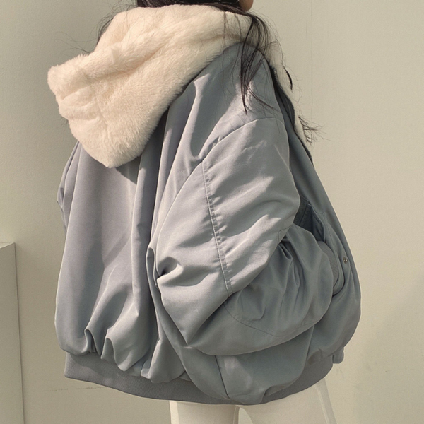 Seitenansicht einer Frau, die eine blaue Wendejacke mit Kapuze, Reißverschluss und Tasche trägt