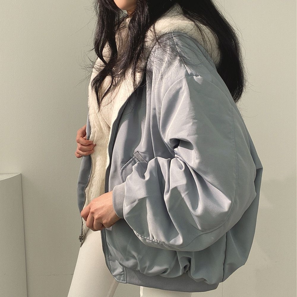Seitenansicht einer Frau, die eine blaue Wendejacke mit Kapuze, Reißverschluss und Tasche trägt