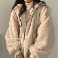 Nahaufnahme einer Frau, die eine beige Wendejacke mit Kapuze, Reißverschluss und Tasche trägt