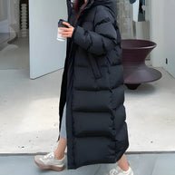 Ein modell, das eine lange schwarz wasser- und winddichte jacke trägt, gehend in einem modernen innenraumraum