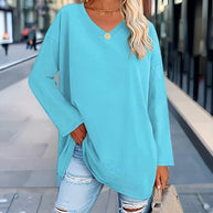 Frau trägt cyanfarbenes Langarmshirt mit V-Ausschnitt und eine Hand in der Tasche