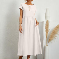Woman in a white flowing summer dress,  standing by a white wall