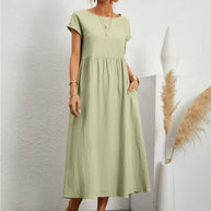 Frau in einem hellgrünen, fließenden Sommerkleid steht vor einer weißen Wand