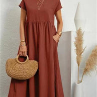 Stilvolle Frau in einem orangefarbenen Sommerkleid mit einer Tasche vor einer weißen Wand.