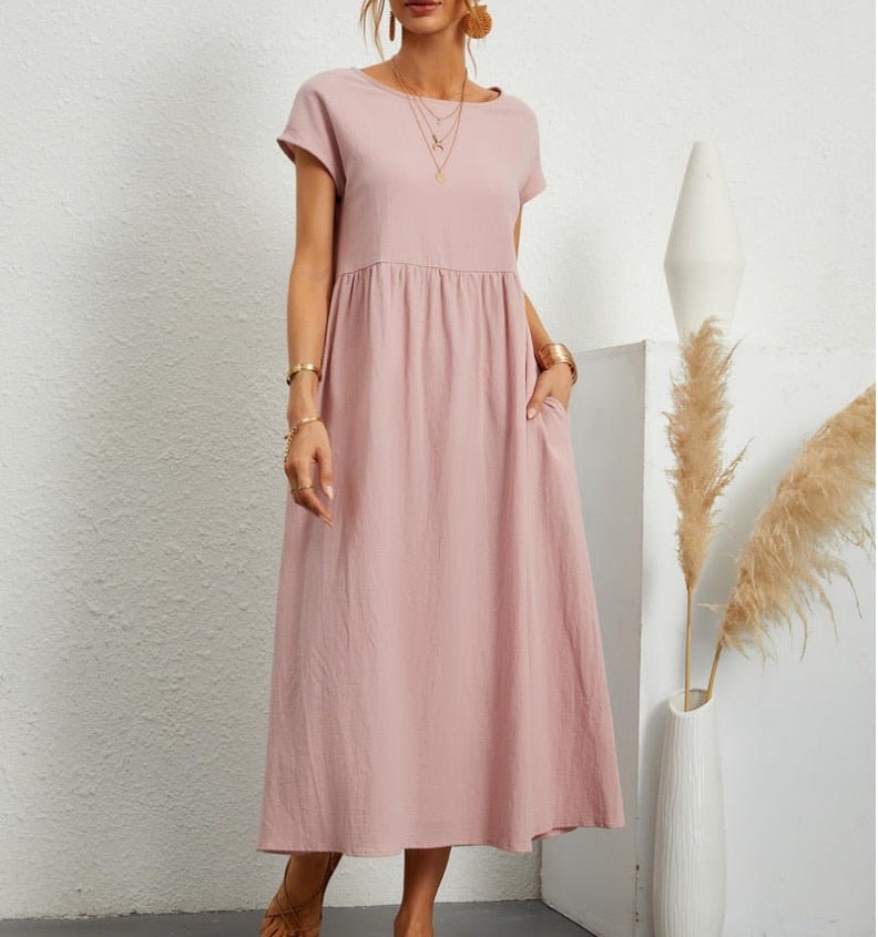 Frau in einem rosa fließenden Sommerkleid steht an einer weißen Wand