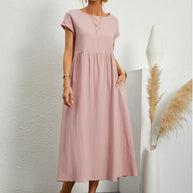 Frau in einem rosa fließenden Sommerkleid steht an einer weißen Wand
