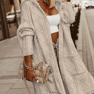 Modische Frau trägt beige Strickjacke, weißes bauchfreies Top, blaue Jeans und hält beige gesteppte Handtasche mit Kette