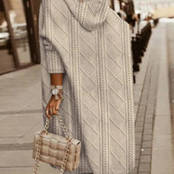 Rückansicht einer Frau, die eine beige Strickjacke mit Kapuze und hellblaue Jeans trägt und eine dazu passende beige gesteppte Handtasche mit Kette hält.